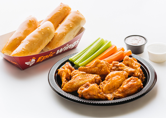 A plate of wings, veggies, sauces, and breadsticks